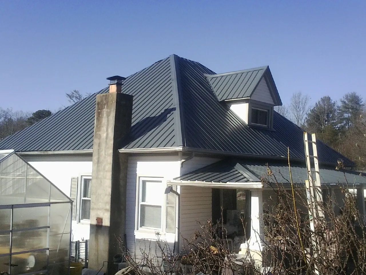 Dark blue standing seam metal roof on a white farmhouse with dormer — Slate & Tile Roof Repair by Roofing Brothers in Polson