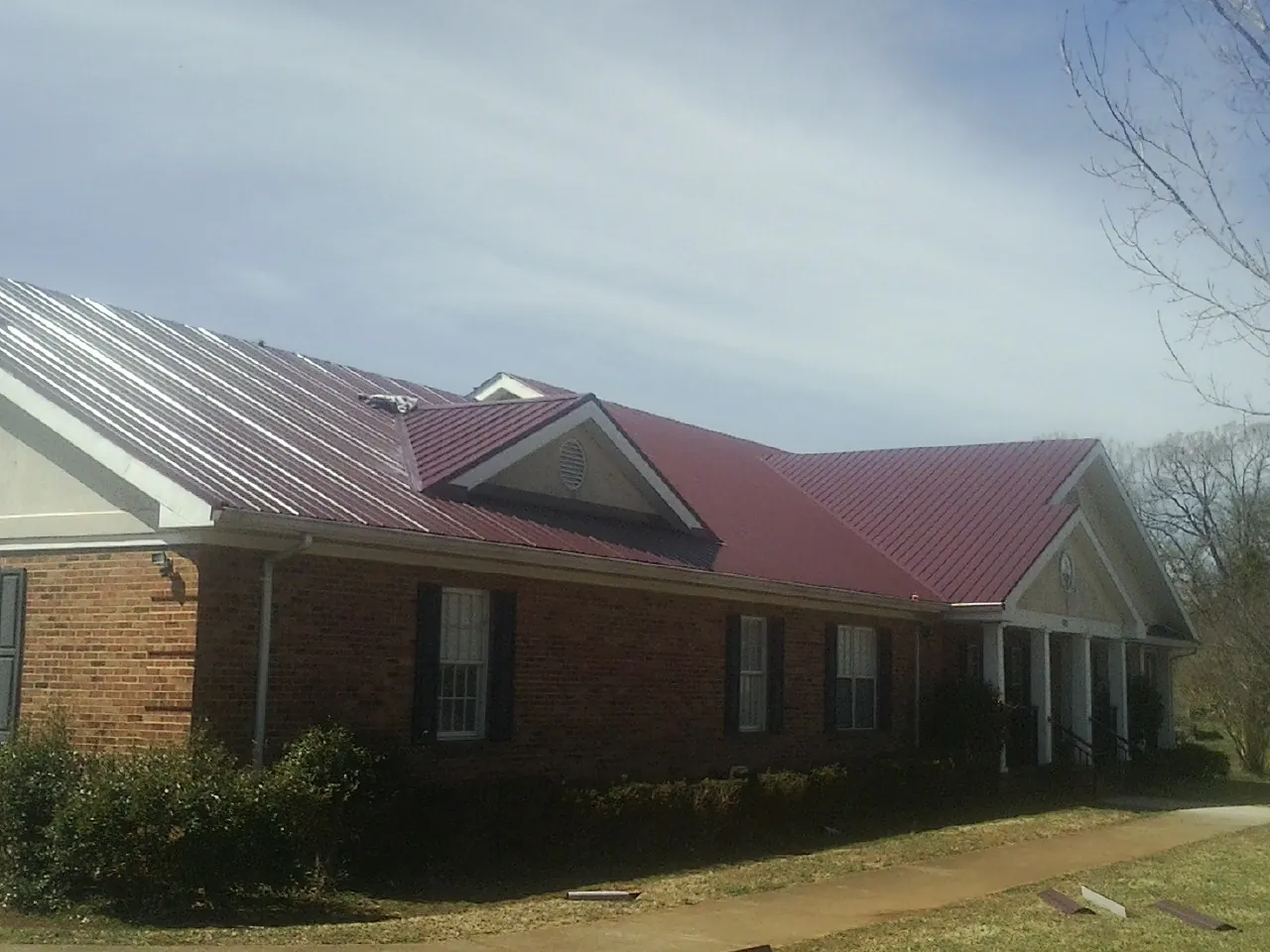 Red metal roof with gabled entries on a long brick building, from a Hail Damage Roof Repair job in Polson