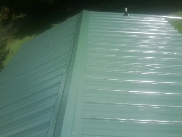 New green metal panels meeting at the ridge of a roof — Flat Roof Repair work by our crew in Polson