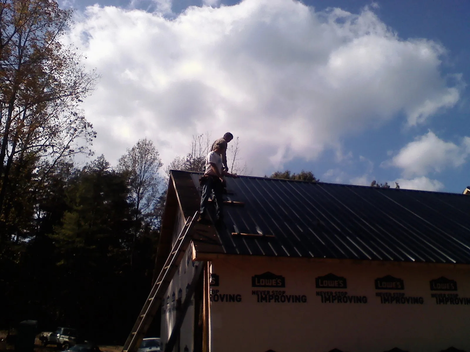 Roofer fastening dark metal panels high against a cloudy sky, from a Roof Inspection job in Polson
